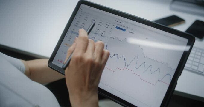 Female Stock Exchange Trader Monitoring and Analyzing Real-Time Stocks, Market Charts in Online Trading App Using Digital Tablet and Stylus. Professional Investment Agent Working in Office. Close Up.