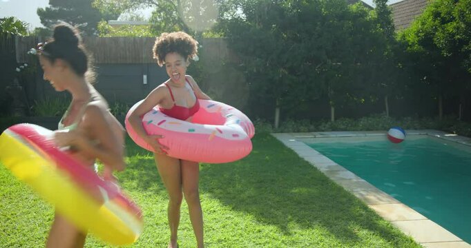 Diverse friends enjoying pool party, laughing and splashing water with colorful floaties