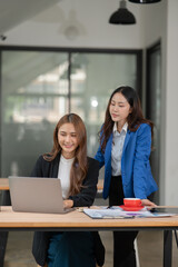 Two Asian businesswomen using laptops, on the table there are graph documents working on business investment.