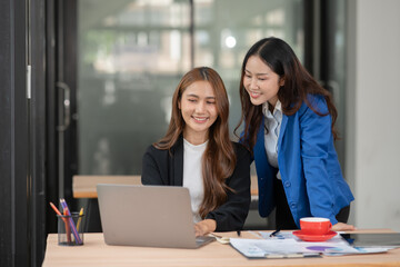 Two Asian businesswomen using laptops, on the table there are graph documents working on business investment.