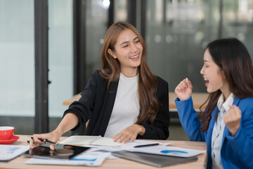 Two Asian businesswomen happily express their joy at the office.