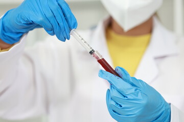 Scientist in laboratory analyzes blood sample using microscope and test tubes. Biotechnology, medicine, and research focus on disease discovery and DNA.