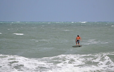 A surfer riding an electric, motor-driven, hydrofoil-equipped surfboard in the ocean at Ponce Inlet...