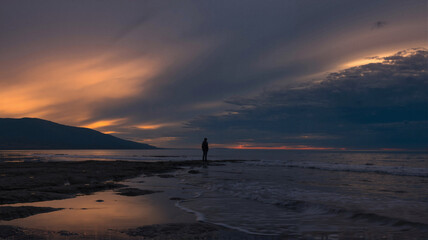 Silhouette of a person walking along the shoreline at sunset  