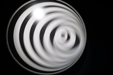 A circular black and white spiral appears in motion due to intentional blur, creating a dizzying optical illusion. 