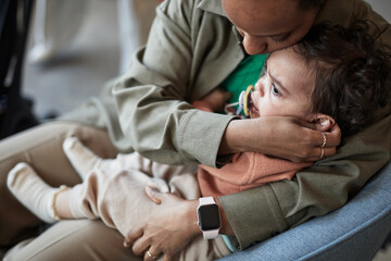Parent cradling and comforting crying toddler sitting on lap with both embracing and protecting...