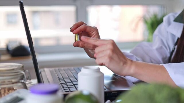 Close-up of doctor's hand holding transparent yellow oval capsule and medical jar for pills and dietary supplements. Vitamin D, omega 3, fish oil.