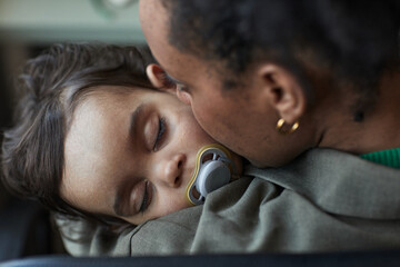 Child sleeping peacefully while being cradled in mother's arms, displaying a tender moment of parental love and affection. Close-up highlights emotional bond between child and parent