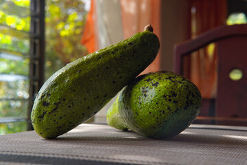 Two avocados on a wooden and glass table with a rustic and country background