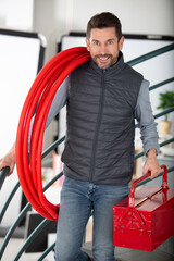 male tradesman with reel of red pipe on his shoulder