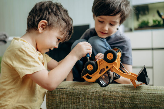 Brothers playing and repairing a toy truck indoors with a screwdriver