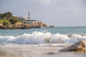 Leuchtturm auf Felsen mit Brandung am Strand