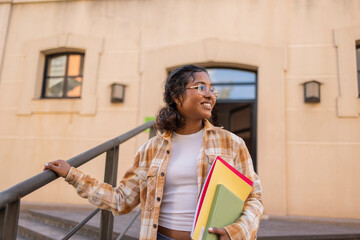 Student smiling while holding books outside a university building
