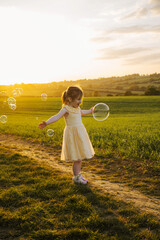 5 years old little toddler girl playing with soap bubbles at sunset