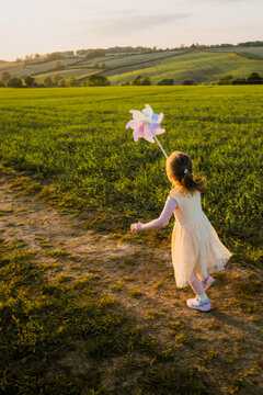Toddler girl running with a windmill at sunset, copy space