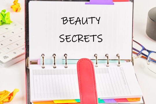 A planner opens to reveal the phrase beauty secrets, surrounded by colorful notes and stationery. This setup highlights organized tips for effective beauty care and self-improvement