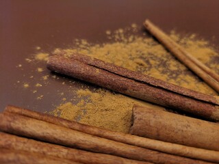 Aromatic cinnamon sticks and powder on a brown background.