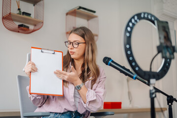 Young businesswoman recording a video podcast and showing a clipboard with blank sheet