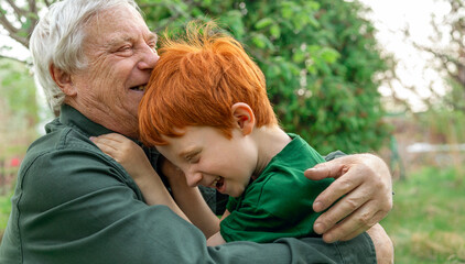 Grandfather hugging his cheerful grandson with ginger hair in the garden