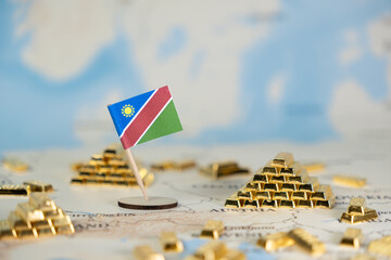 Namibian flag pin among shiny gold bar stacks on a blurred world map, symbolizing national wealth,...