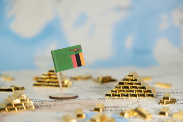 A miniature Zambian flag stands among golden bars on a world map, symbolizing national wealth,...