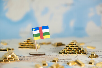 Central African Republic flag standing beside gleaming gold bar piles on a world map, representing...