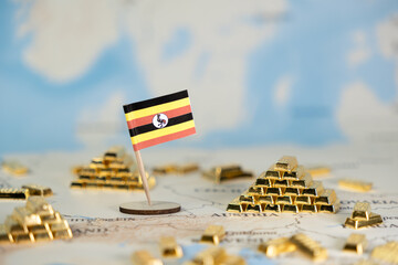 Ugandan flag standing amidst many shiny gold bar stacks on world map, symbolizing global economy,...