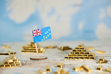 Tuvalu flag and miniature gold bars placed on a world map, symbolizing national wealth, global...