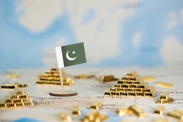 Miniature Pakistan flag and gold bars on a world map symbolize national wealth, economic growth, and global finance, offering ample copy space