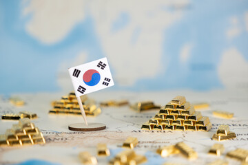 Small South Korean flag stands on a detailed world map surrounded by numerous miniature golden...