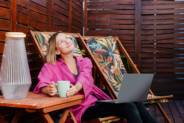 Woman enjoying leisure time with a laptop on a sunny terrace