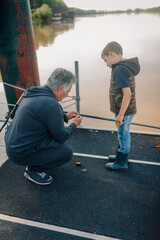 Grandfather teaching grandson how to fish on a lake pier
