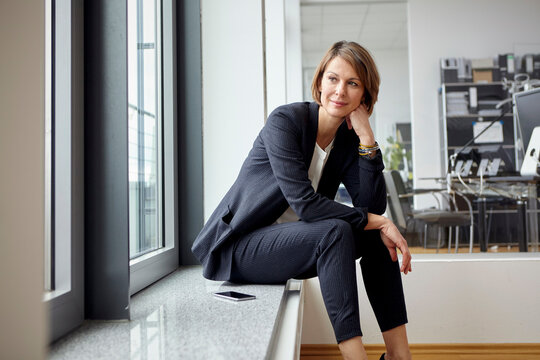 Businesswoman sitting by a window in an office looking thoughtful