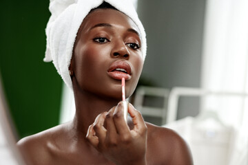 Woman applying lip gloss in a beauty routine at home during the daytime with natural light...