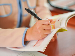Closeup of teacher or student's hand writing, taking notes in classroom at kid school. Reading,...