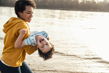 Playful mother carrying son while playing by lake on sunny day