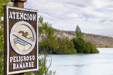 Warning sign prohibits swimming in a visible river surrounded by vegetation and low...