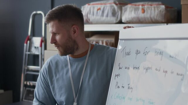 Handheld shot of young Caucasian man standing by flipchart discussing workplan with female African American volunteer at center