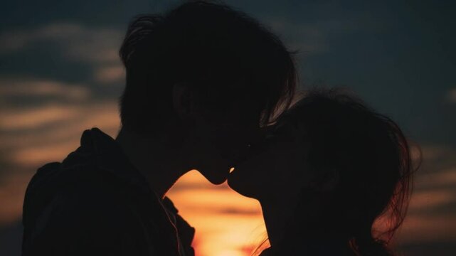 Romantic Evening Embrace: A tender moment of two lovers silhouetted against a breathtaking sunset, their faces inches apart as they share a kiss, their forms enveloped in a warm glow.