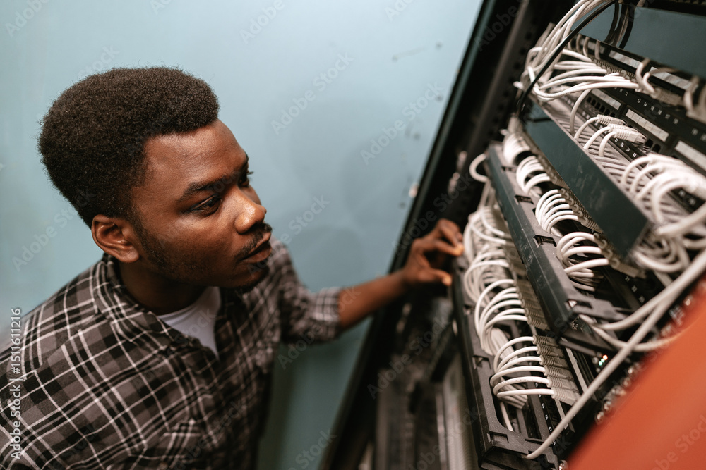 Poster young technician working on networking cables in a server room during daylight hours