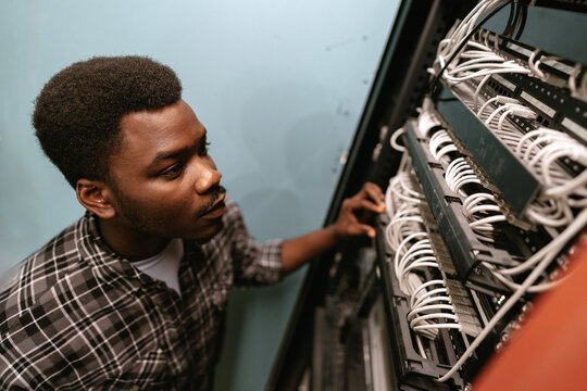 Young technician working on networking cables in a server room during daylight hours