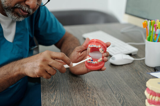 Mature Doctor Demonstrating How to Clean Teeth with Braces using Model