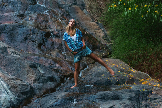 Woman posing playfully on rocky stream with greenery backdrop
