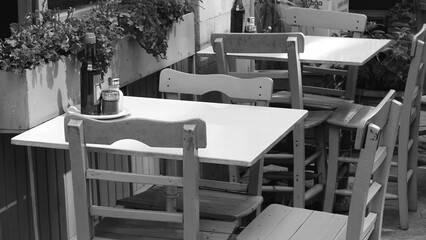 Black And White Photo Of Empty Outdoor Cafe Tables In A Quiet Street Captured From A Street Level Perspective Creating A Timeless Urban Atmosphere