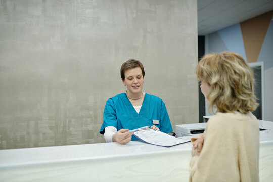 Young Receptionist Giving Medical Agreement to Patient of Clinic