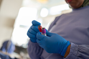 Close-up of medical worker in blue gloves holding blood sample tubes. Focus on healthcare,...