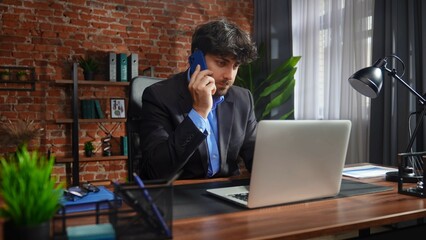 Businessman in Office Talking on Phone and Using Laptop