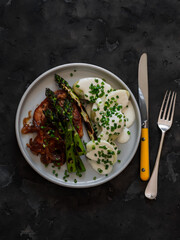 Delicious lunch and dinner - pork chop, asparagus, potatoes with yogurt sauce on a dark background, top view