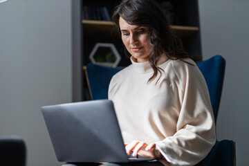 Young adult female using laptop in modern home office setting