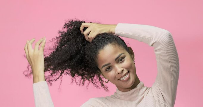 Latin model making a ponytail on pink background in slow motion. Beautiful latin model